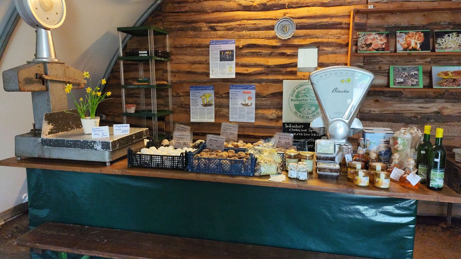 Verkaufstheke im Hofladen: Kisten mit Champignons und Shiitake, Gläser, Honig und Apfelwein vor einer Holzwand, rechts die alte Bizerba-Waage